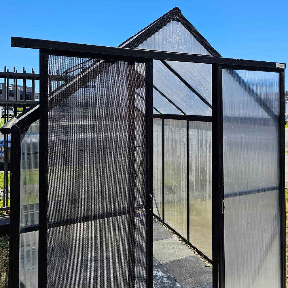 Modern Winter Gardenz greenhouse with black metal frame, translucent panels, and sliding screen door
