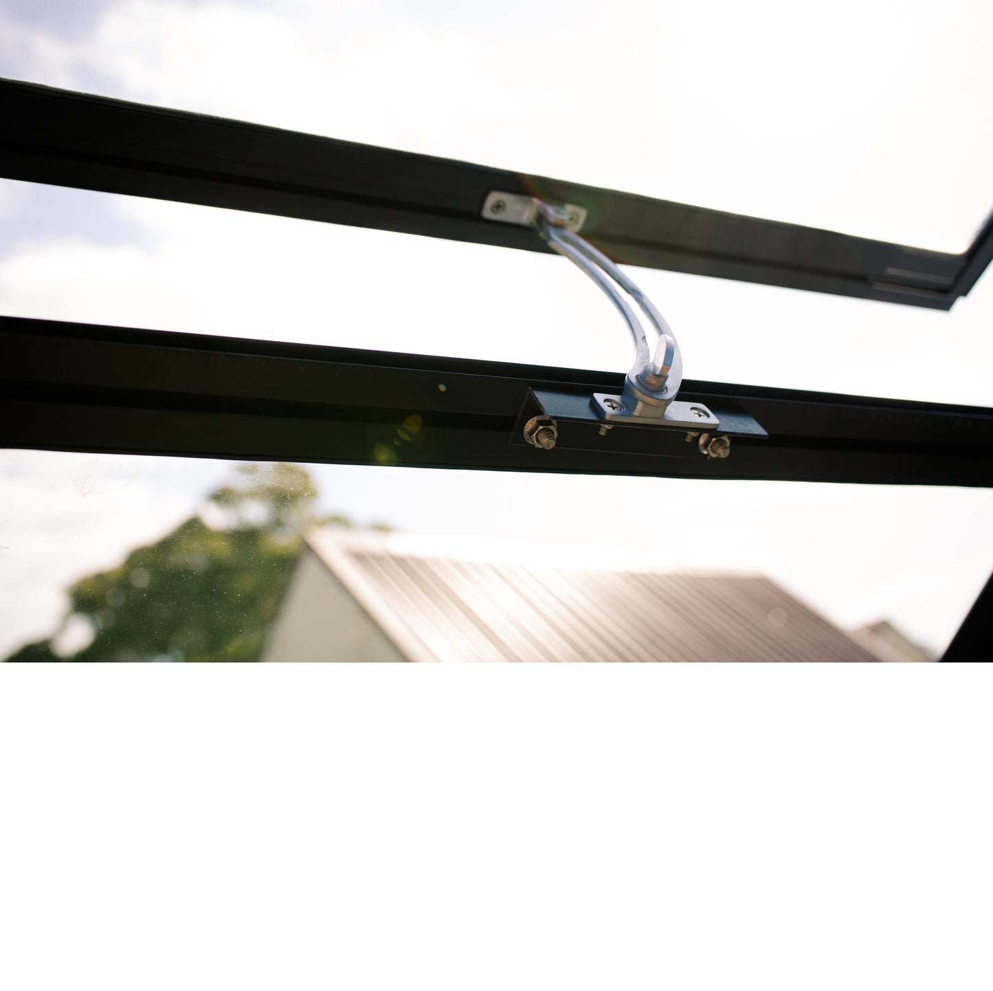 Close-up of a black metal window vent opener mechanism with attached metal arm on an open window