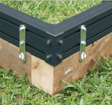 Foundation flush mounting kit securing black raised garden bed corners to wooden base on grass