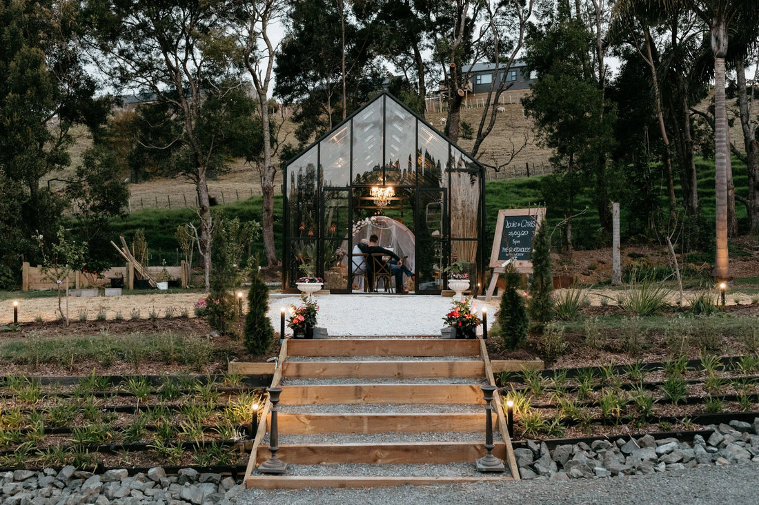 Couple sitting inside a glasshouse wedding venue with garden path and lit steps in a rural setting