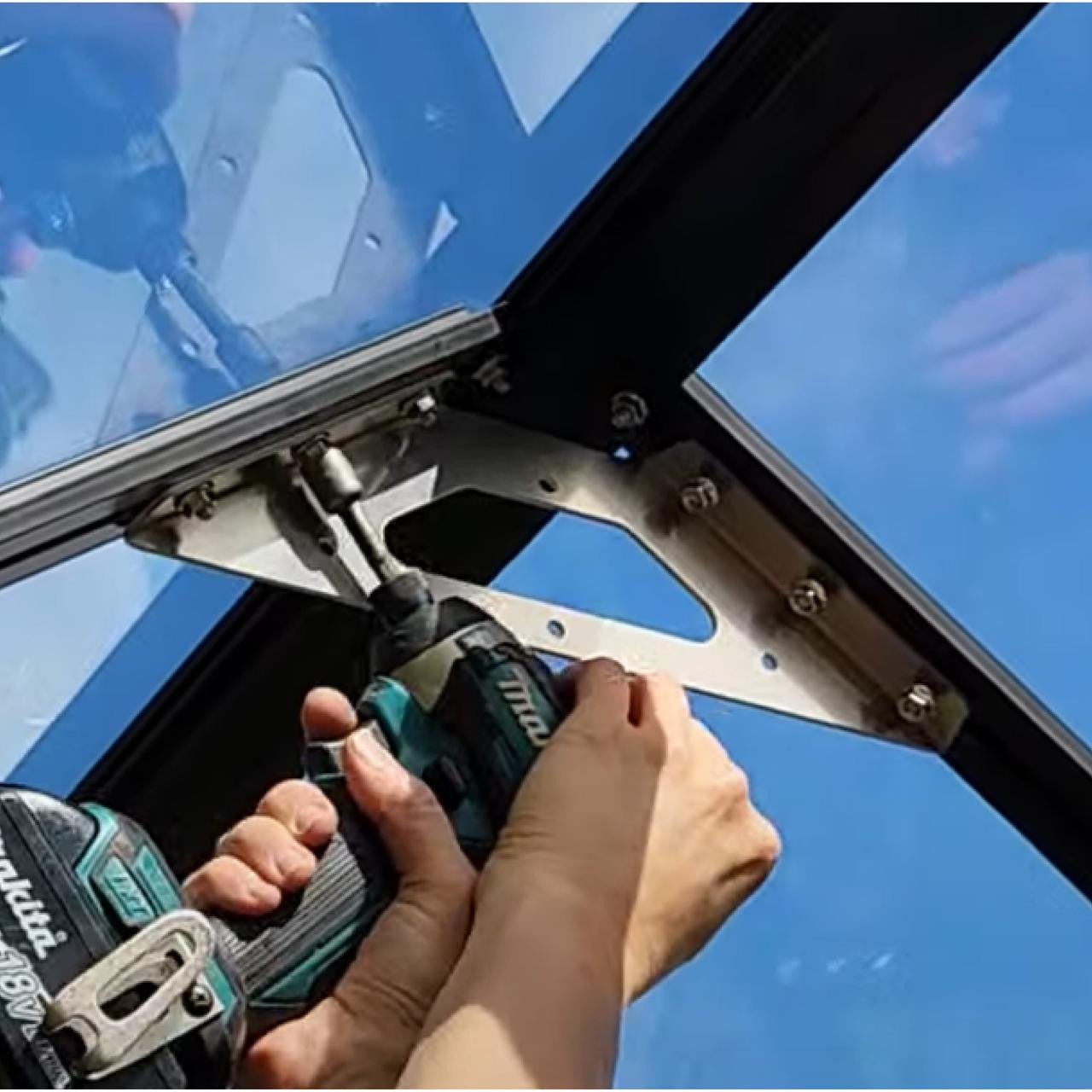 Person using Makita cordless drill to install metal roof brace bracket on glass roof panel