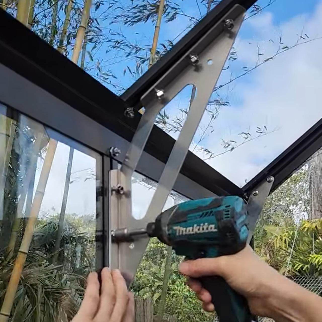 Installing a stainless steel eave brace on a black framed glass structure using a Makita power drill outdoors
